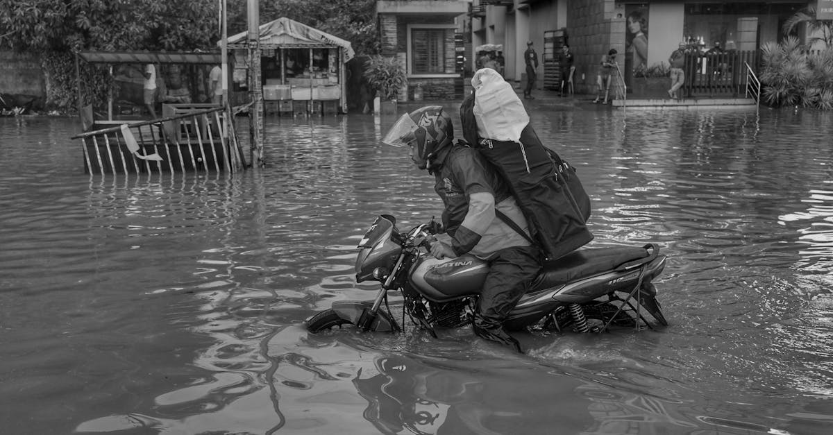 A motorcyclist in gear tackles urban flooding in Kolkata, India, highlighting a natural disaster.