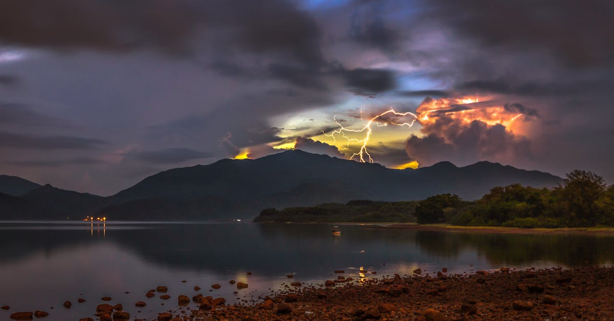 A stunning lightning storm illuminates the sky over a calm mountain lake during twilight.