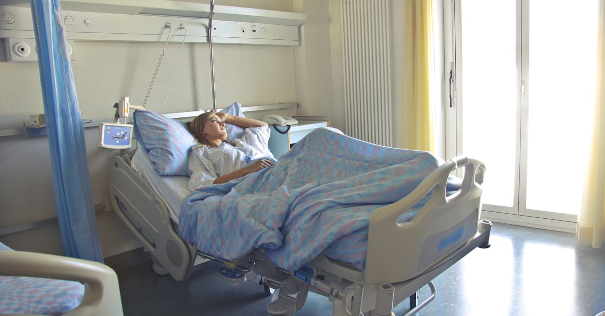 A woman lying in a hospital bed in a bright, softly lit room, appearing to rest or recover.