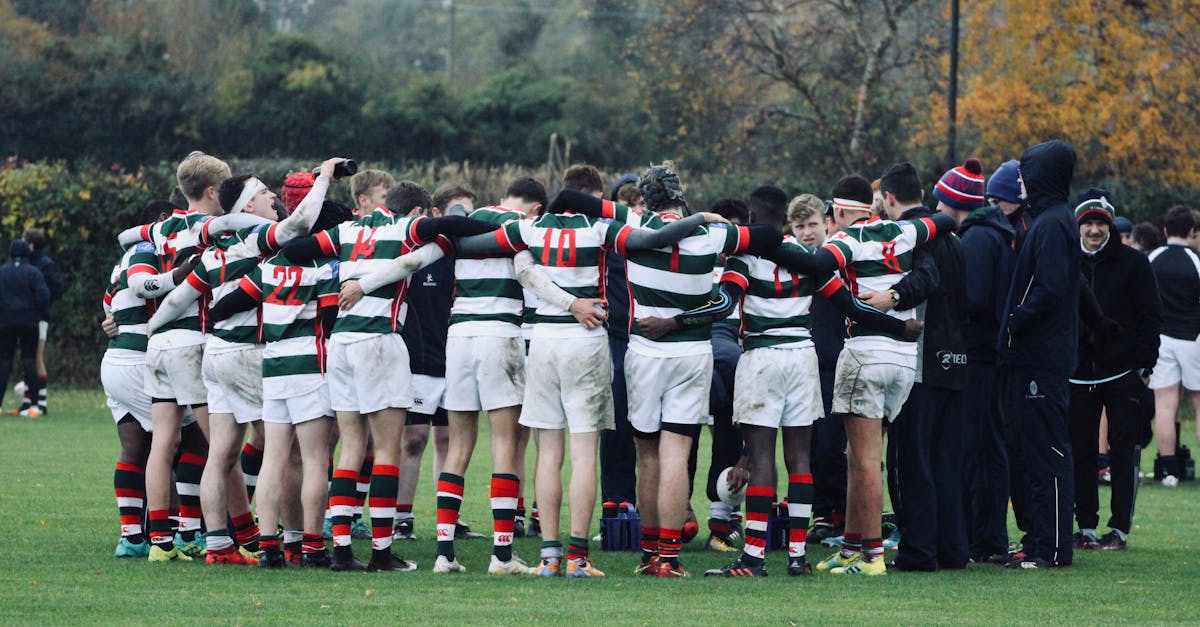 Rugby players in striped jerseys huddle during a game on an autumn field.