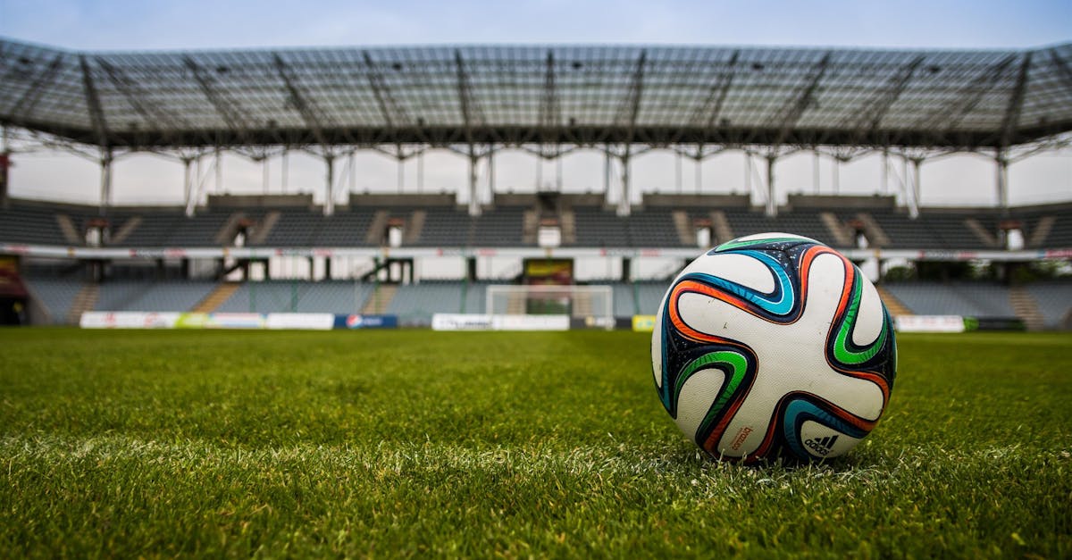 Close-up of a soccer ball on a lush grass field with an empty stadium in the background.
