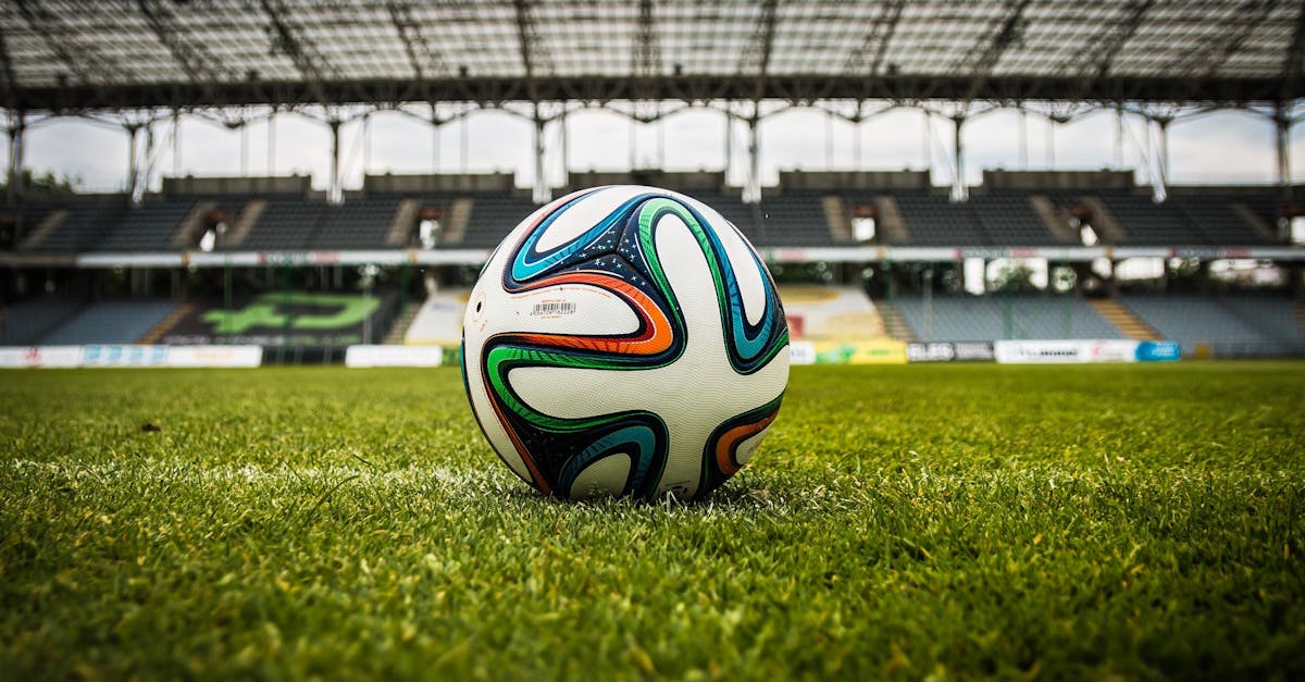 A vibrant soccer ball rests on a lush green field inside an empty stadium, capturing the essence of sports.